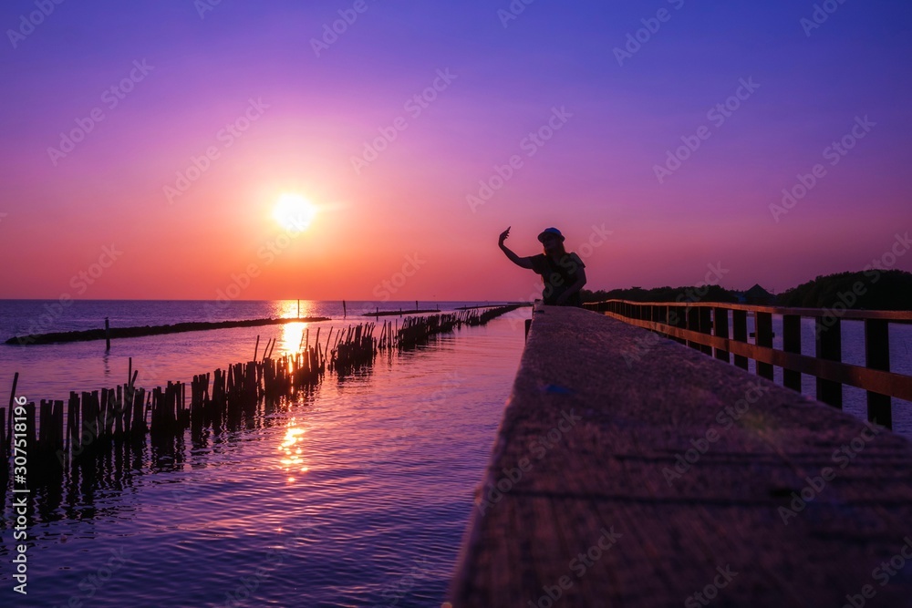 A woman silhouette standing Selfie on wooden pier at the sea with beautiful cloudy sunset. A woman silhouette standing Selfie on wooden pier at the sea with beautiful cloudy sunset.