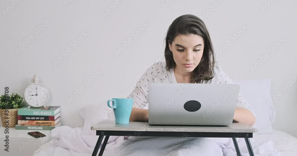 Woman in bed working on laptop. Caucasian woman, looking at laptop. Wide shot with copy space.