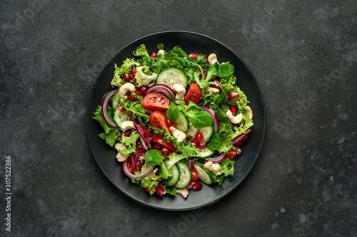 Salad with pomegranate, tomatoes, fresh cucumbers, onions, sesame seeds and cashew nuts, spices on a stone background. Healthy vegetarian food.