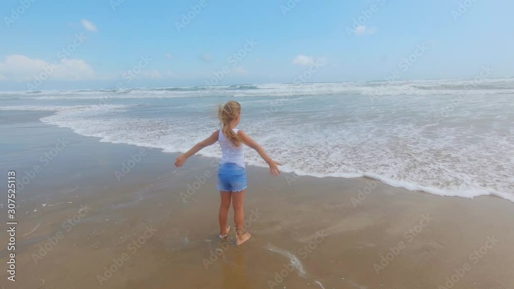 Girl looking at sea with wind in her hair. Beautiful blond hair develops in the wind and she is happy. Child by the sea with waves. Girl looking at sea with wind in her hair. Beautiful blond hair develops in the wind and she is happy. Child by the sea with waves.