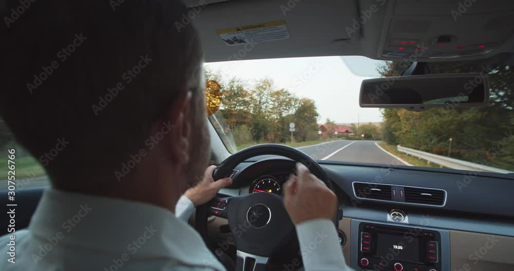 Shot for animation. Back closeup view of adult bearded man in sunglasses and white shirt driving car across the road with day light on background. Tapping finger.Navigation app online. Successful life Shot for animation. Back closeup view of adult bearded man in sunglasses and white shirt driving car across the road with day light on background. Tapping finger.Navigation app online. Successful life