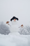 Snowman and snow day. Snowman with a bag of gifts. Funny snowman with a carrot instead of a nose and in a warm knitted hat on a snowy meadow on a blurred snow background. Snowmen.