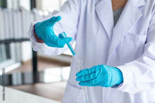 scientist wearing lab coat and gloves taking a sample in syringe while working over scientific experiment in laboratory