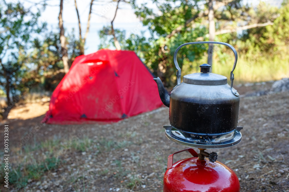Cooking camping kettle on a red gas bottle. Tent and sea background