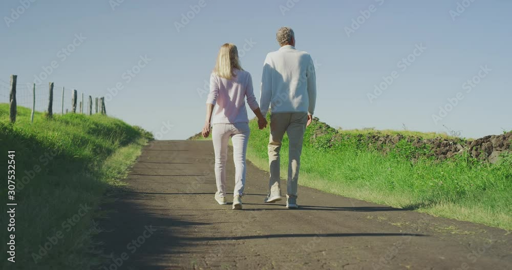 Healthy active older couple taking a walk outdoors holding hands together, elderly mature couple enjoying their retirement outdoors Healthy active older couple taking a walk outdoors holding hands together, elderly mature couple enjoying their retirement outdoors