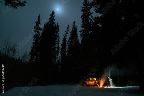 People camping under starry sky near campfire in winter in remote landscape in Canada