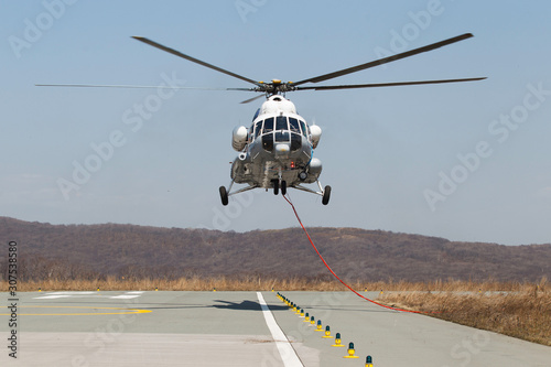 Teachings of the Ministry of Emergencies. Emergency firefighter helicopter takes off from a helipad on a background of a burning field.