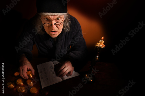 Old Scrooge busy counting his gold coins beside a candle