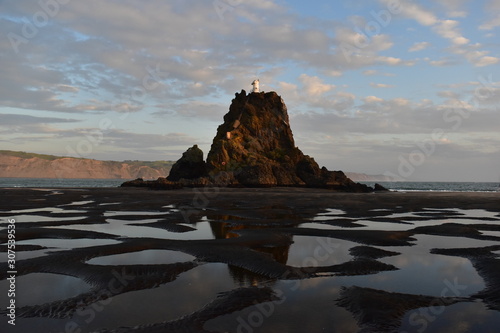 Puddles in the sand with isolated island cliff and lighthouse