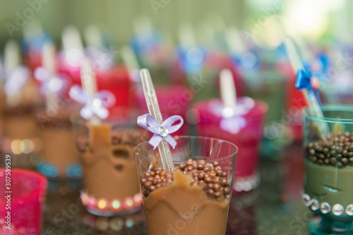 Closeup of transparent cups with chocolate and plastic spoon with blue bow on children's party. Selective focus.