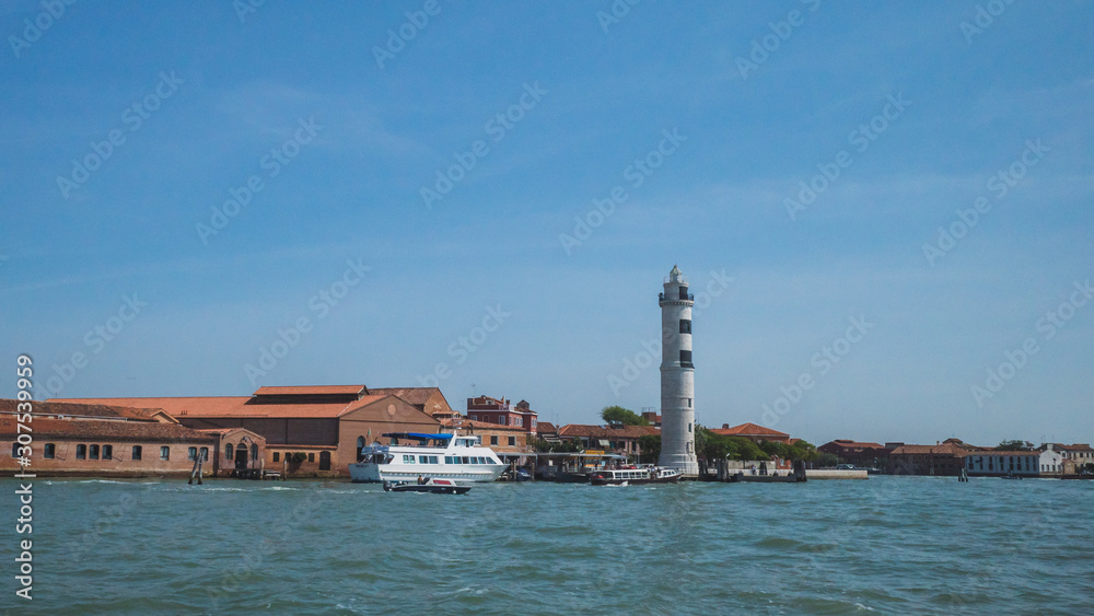 Lighthouse and buildings by water, in Murano, Venice, Italy