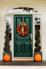 Green front door with fall autumn wreath with leaves and topiaries and pumpkins