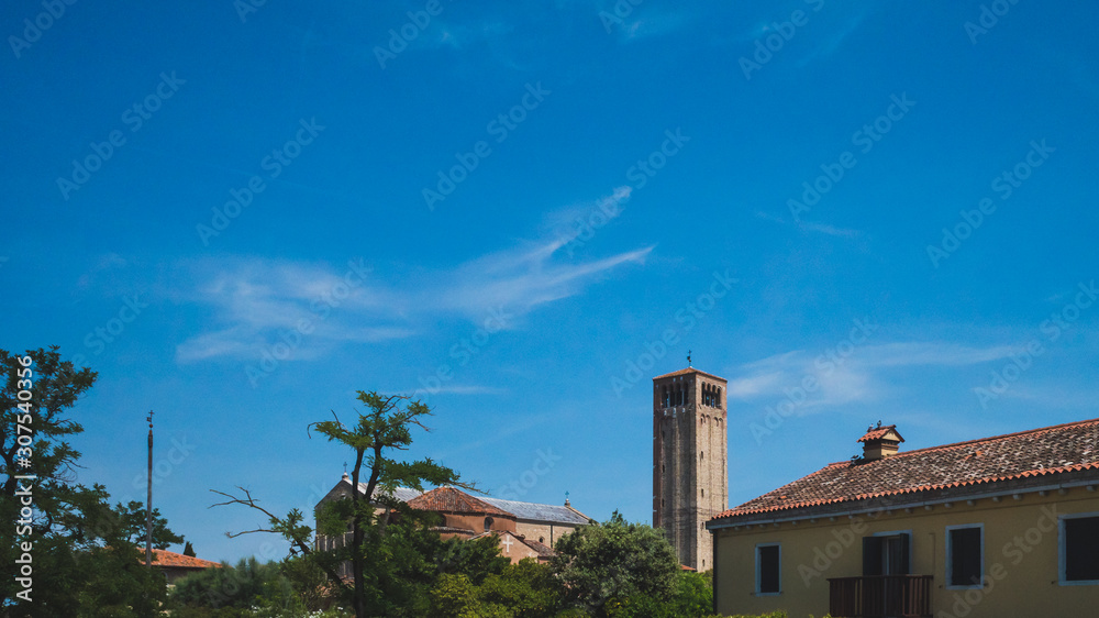 Bell tower of Cathedral of Santa Maria Assunta over buildings and trees in Torcello, Venice, Italy