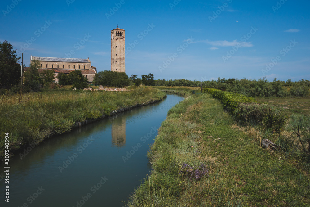 Cathedral of Santa Maria Assunta and bell tower by river on island of Torcello, Venice, Italy
