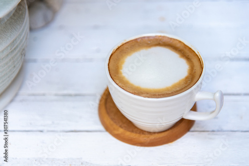 A cup of hot latte on a white wooden table