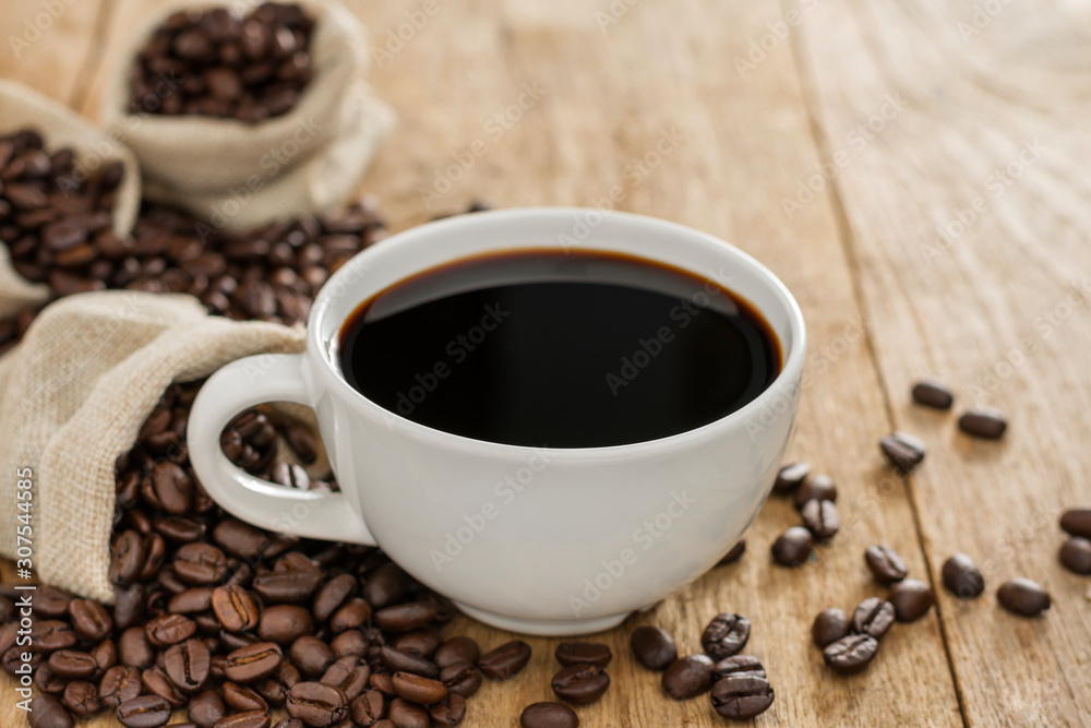 Black coffee in a white coffee cup and roasted coffee beans placed on a wooden table top view Black coffee in a white coffee cup and roasted coffee beans placed on a wooden table top view