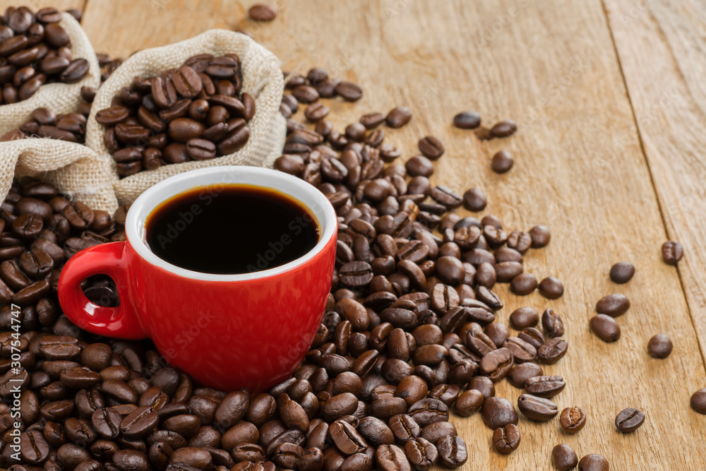 Black coffee in a red coffee cup and roasted coffee beans placed on a wooden table top view Black coffee in a red coffee cup and roasted coffee beans placed on a wooden table top view