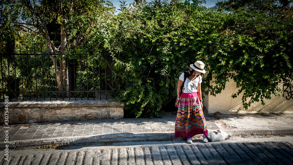 Asian woman in white t-shirt in Athens in white hat and sarong looking down at cat Asian woman in white t-shirt in Athens in white hat and sarong looking down at cat