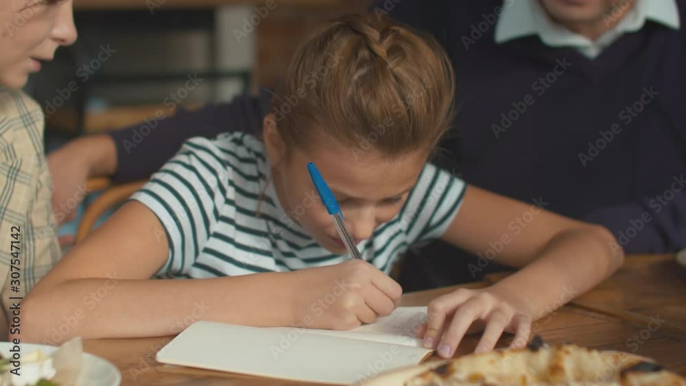 Pretty girl write something at lunch, parents sit with her and help Pretty girl write something at lunch, parents sit with her and help