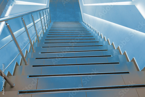Modern classic stairs for descent down and rise up, illuminated by blue light. Dramatic background for creative. Soft selective focus.