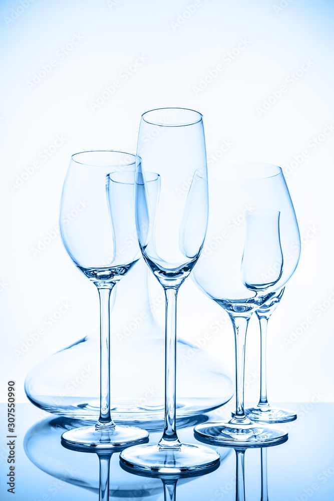 Glassware selection with wine, champagne, liquour glasses and decanter on the light background in blue toning. Fine cristal glassware concept. Vertical.