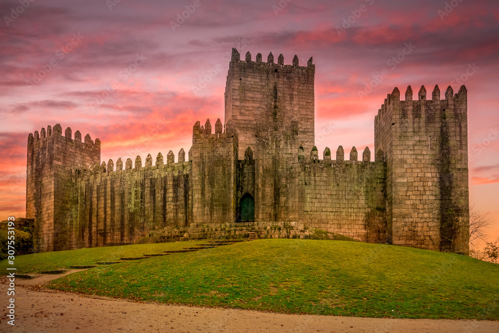 Aerial view of well-preserved medieval buildings hilltop, 10th-century Guimarães Castle with stunning sunset orange red purple sky