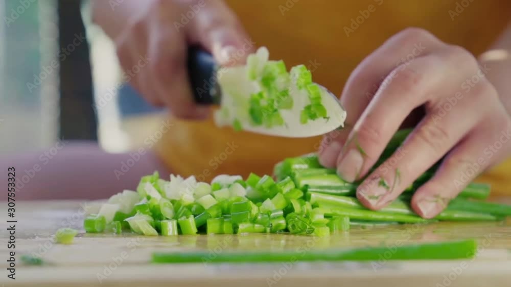 Female cook chopping a bunch of fresh green onions on a wooden cutting board. Slow motion Female cook chopping a bunch of fresh green onions on a wooden cutting board. Slow motion