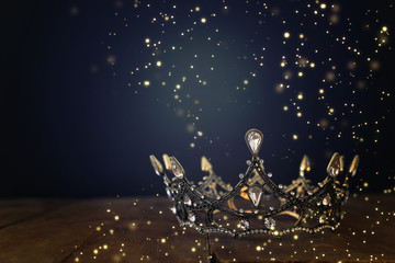 low key image of beautiful queen/king crown over wooden table. vintage filtered. fantasy medieval period. Glitter sparkle lights