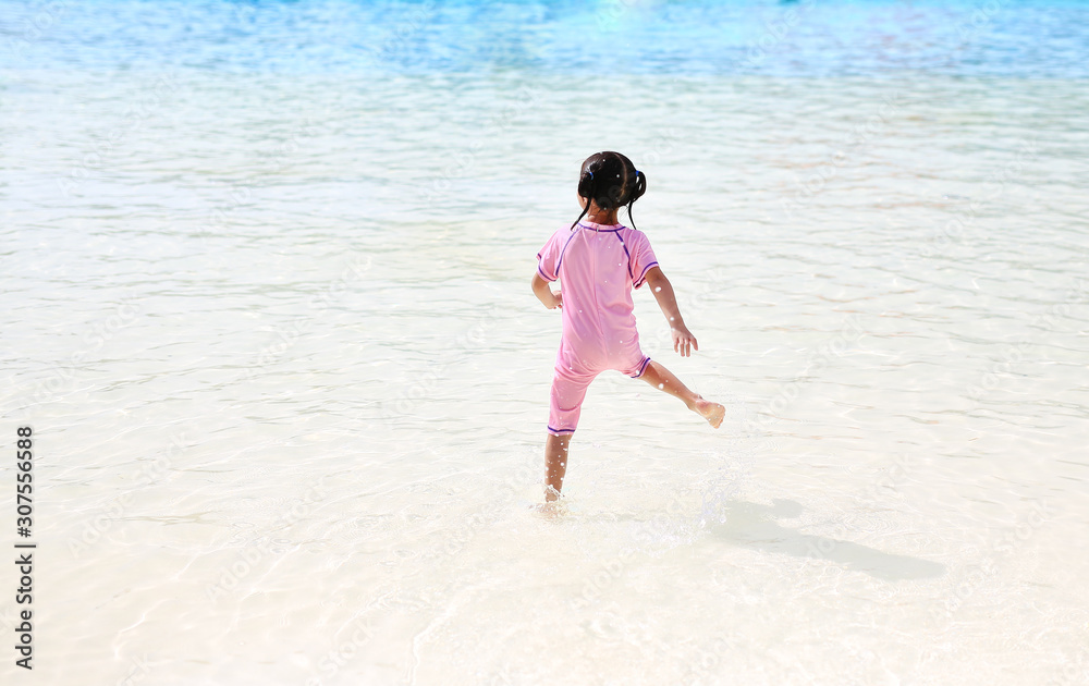 Little Asian child girl having fun and running into aqua park on holidays. Back view kid enjoys in big swimming pool outdoor. Little Asian child girl having fun and running into aqua park on holidays. Back view kid enjoys in big swimming pool outdoor.