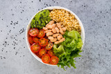 A plate of fresh salad with white beans, bulgur, cherry tomatoes and avocado, decorated with black sesame seeds. Horizontal photo with copy space, top view