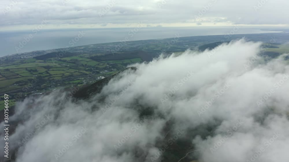 Aerial view of mountain peak in clouds against blue sky. Mountain landscape surrounded by green fields. Sugarloaf Mountain, Wicklow, Ireland. 4K UHD Aerial view of mountain peak in clouds against blue sky. Mountain landscape surrounded by green fields. Sugarloaf Mountain, Wicklow, Ireland. 4K UHD
