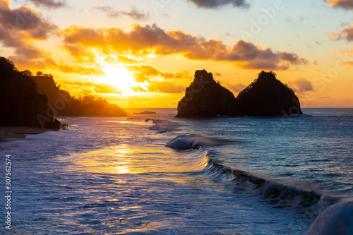 Beautiful sunset in Fernando de Noronha, Brazil. Taken from a mountain peak called Pedra do Bode. Waves crashing at shore with sun setting at distance near Two Brothers Mountain.