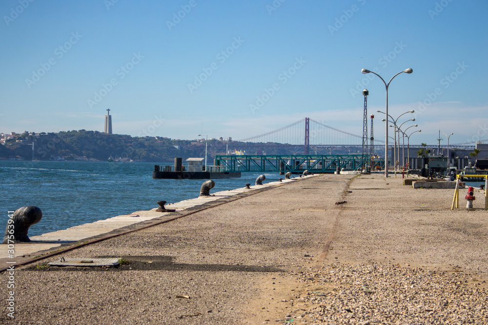 Lisbon, Portugal - 10/20/2018: Empty embankment in Lisbon on sunny summer day. Port and riverside with lanterns and bridge on background. Lisbon landmark. Quay in Lisboa.