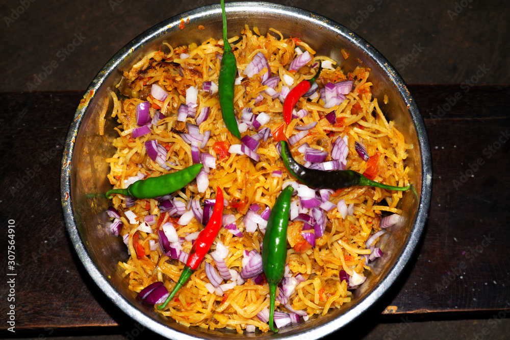 Bowl of fried noodles recipe with onion slices, red tomatoe slices, red and green pepper and vegetables on wooden background top view in indian village