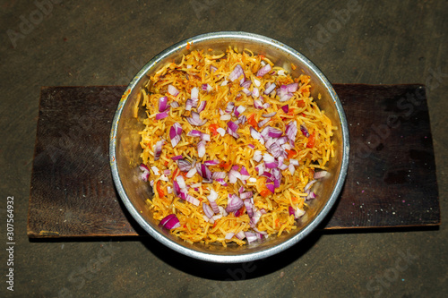 Bowl of fried noodles recipe with onion slices, red tomatoe slices, red and green pepper and vegetables on wooden background top view in india