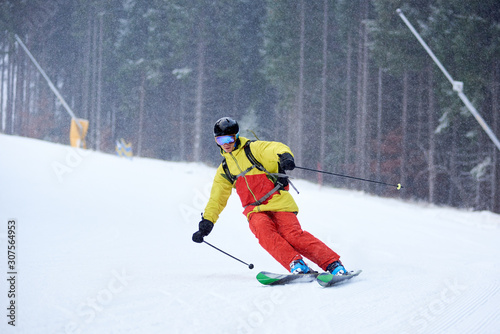 Young skier performing skiing trick. Ski training in dense snowfall in mountains. Carving skiing technique. Trees and dark forest on background. Winter activities, freestyle, adventure, thrill concept