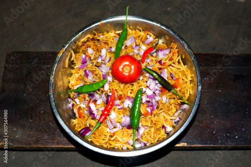 Bowl of fried noodles recipe with onion slices, red tomatoe, red and green pepper and vegetables on wooden background top view in india