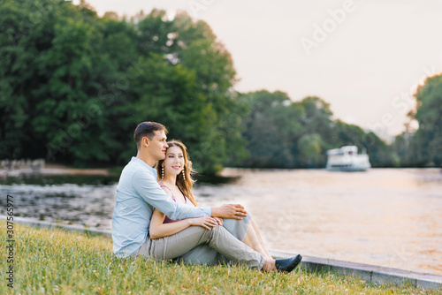 A young couple in love, a guy and a girl are sitting on the shore of the lake, happy and smiling. First date. Valentine's day