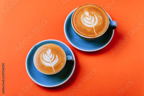 Cyan cappuccino coffee cups over orange background. Top view flat lay with copy space