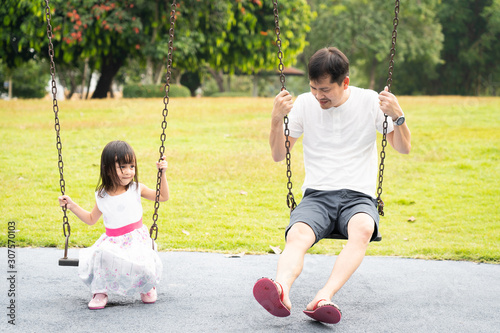 Asian father and daughter are playing the swing together in the playground of the park with happy moment, concept of outdoor activity for children in the family lifestyle. © Sukjai Photo