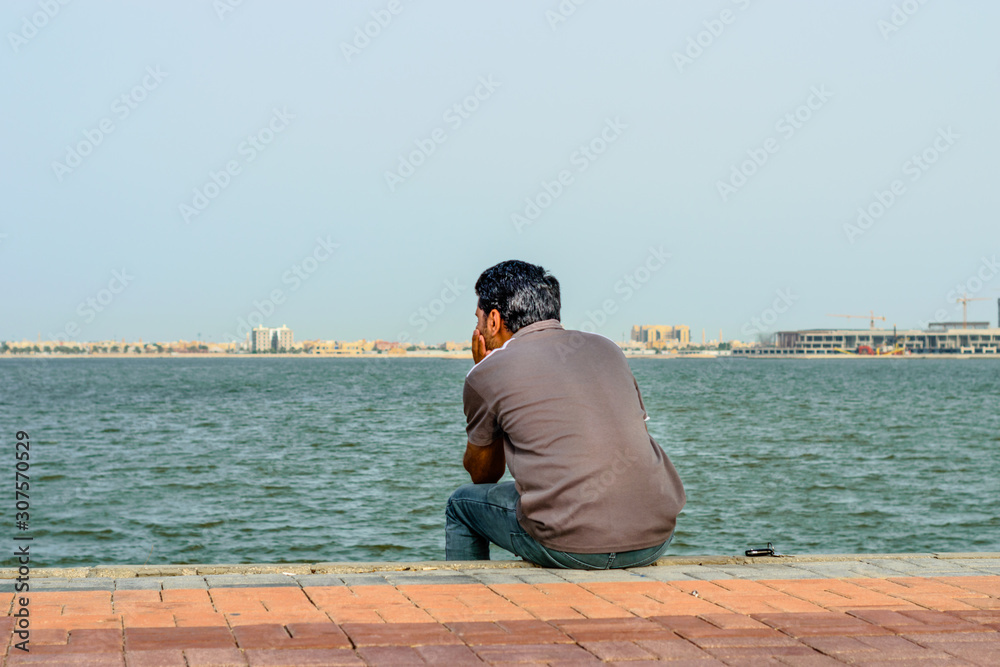 a lonely man is sitting on the rocks after divorce at seaside wearing grey t shirt and blue jeans in the bright cloudy day a lonely man is sitting on the rocks after divorce at seaside wearing grey t shirt and blue jeans in the bright cloudy day