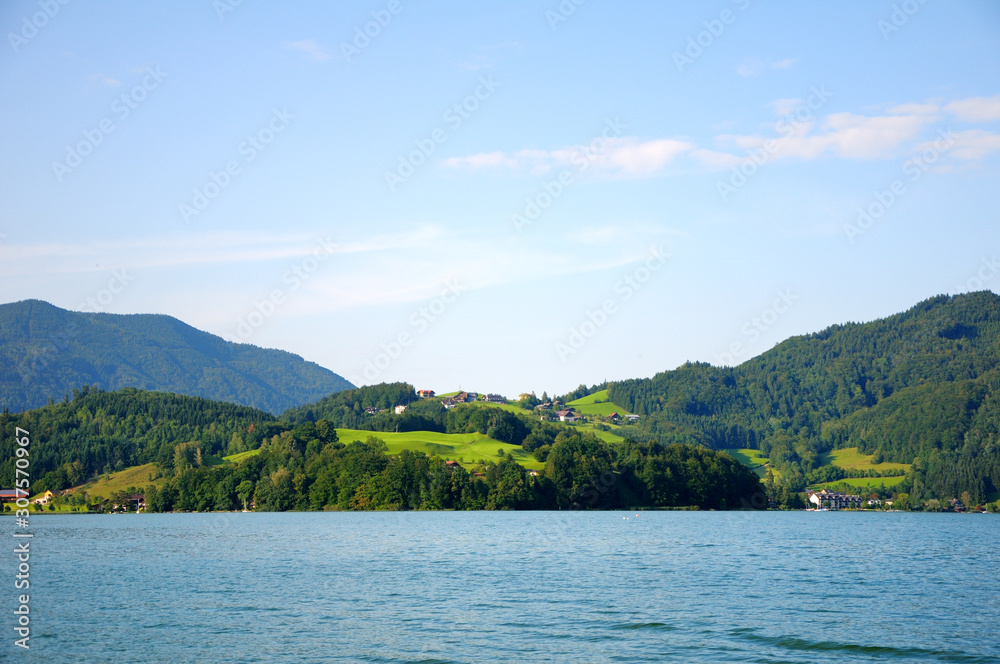 Houses on a hill by the lake. Mountains with forest in the background. Beautiful clear sky, summer day.
