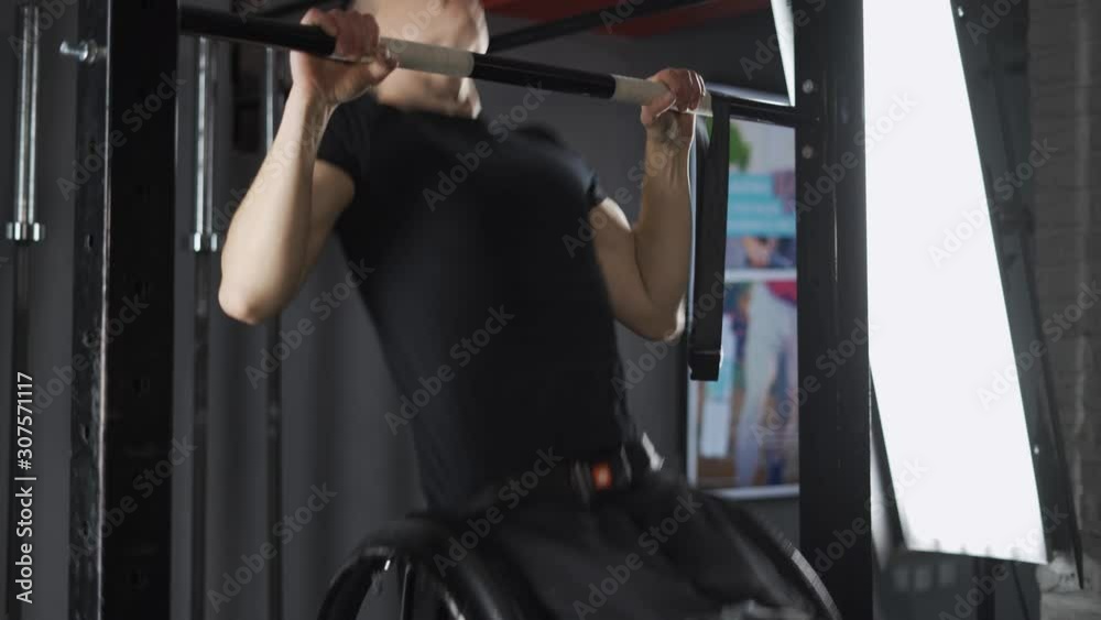 Workout, young disabled athlete in wheelchair performs pull-ups on the horizontal bar, gym training and physical activity, people with disabilities. Workout, young disabled athlete in wheelchair performs pull-ups on the horizontal bar, gym training and physical activity, people with disabilities.