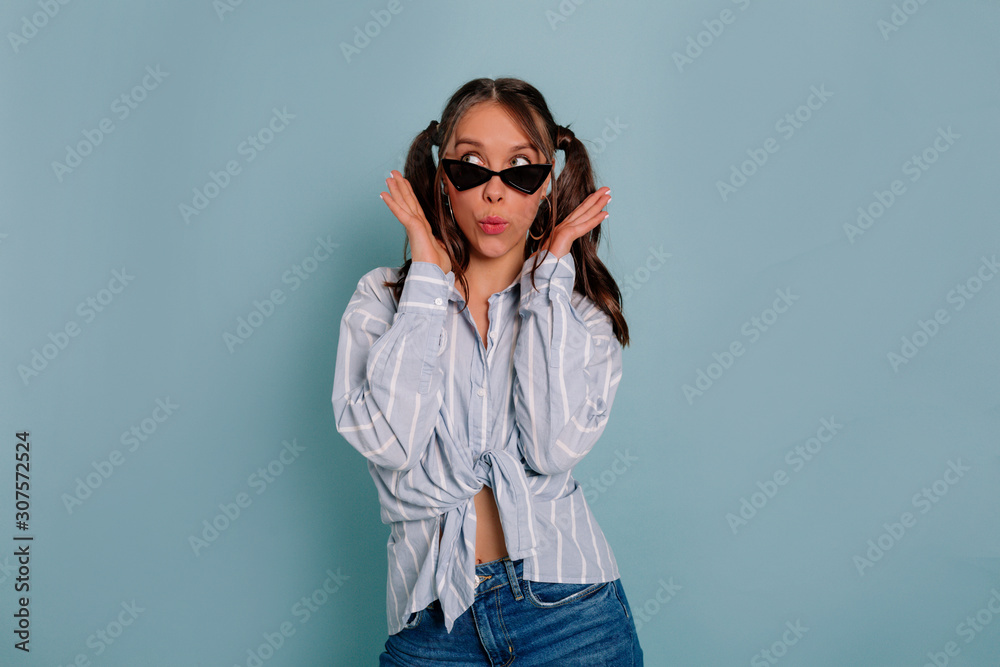 Happy funny lady with surprised emotions looking at camera wearing black sunglasses over blue background Happy funny lady with surprised emotions looking at camera wearing black sunglasses over blue background