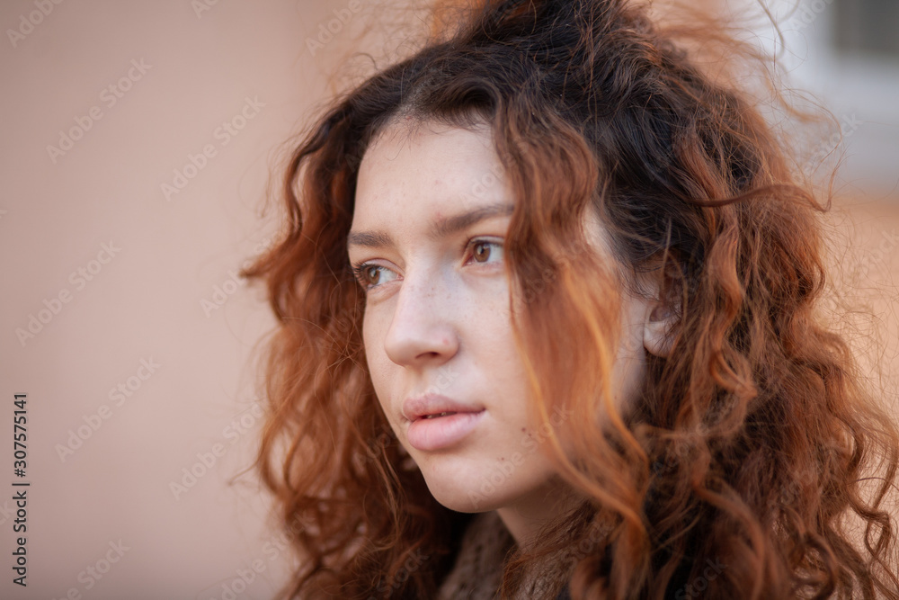 Dreaming young woman with spectacular curly red ginger hair looking at camera posing outdoor in downtown street. Female portrait. Dreaming young woman with spectacular curly red ginger hair looking at camera posing outdoor in downtown street. Female portrait.