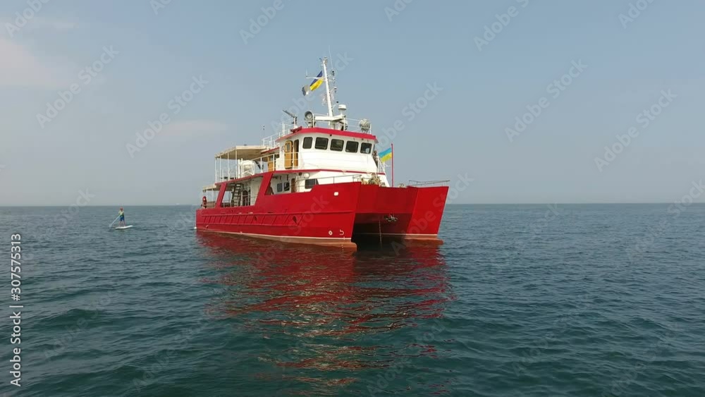 Aerial view. Research vessel drifts in middle of the ocean/sea. Red catamaran under the Ukrainian flag Aerial view. Research vessel drifts in middle of the ocean/sea. Red catamaran under the Ukrainian flag