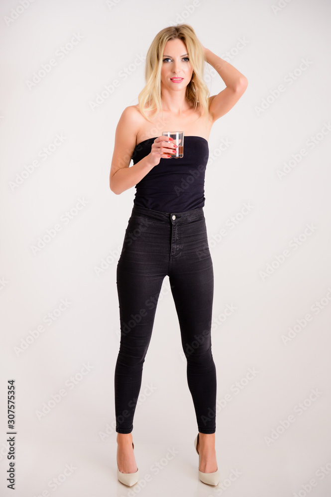 The concept of alcoholic relaxation. Full-length portrait of a pretty woman model with excellent make-up, beautiful hair on a white background standing with a glass of whiskey in her hands. The concept of alcoholic relaxation. Full-length portrait of a pretty woman model with excellent make-up, beautiful hair on a white background standing with a glass of whiskey in her hands.