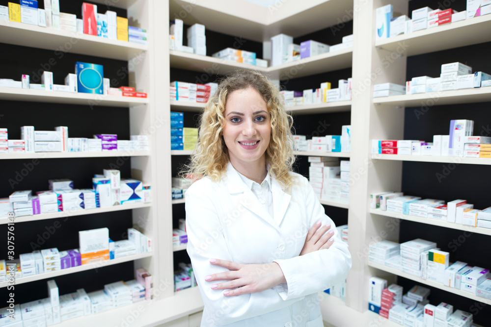 Portrait of female pharmacist in drug store standing in front of shelves with medications. Portrait of female pharmacist in drug store standing in front of shelves with medications.
