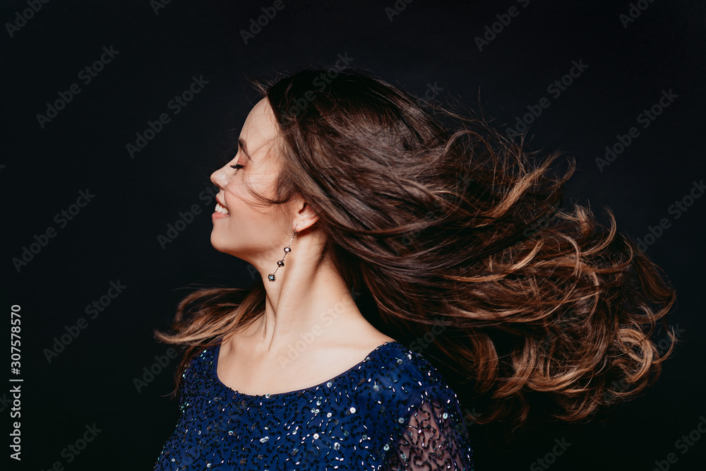 Young beautiful curly women in blue glitter dress on dark background. Fly hairs. Copyspace. Concept celebration Young beautiful curly women in blue glitter dress on dark background. Fly hairs. Copyspace. Concept celebration