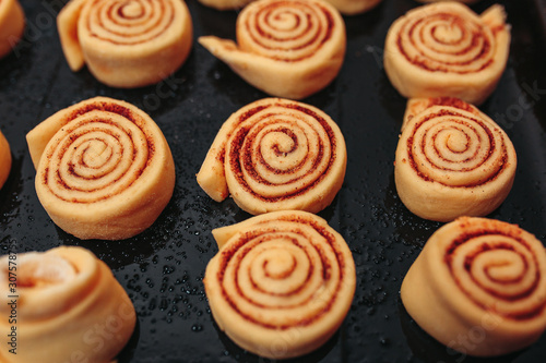 Unbaked cinnamon rolls on the black baking pan on the orange background. Macro unbaked cinnamon rolls.